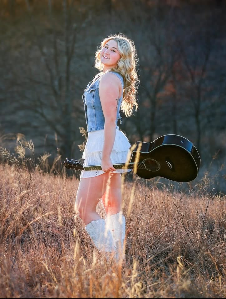 Briella Steiner standing outdoors with a black guitar